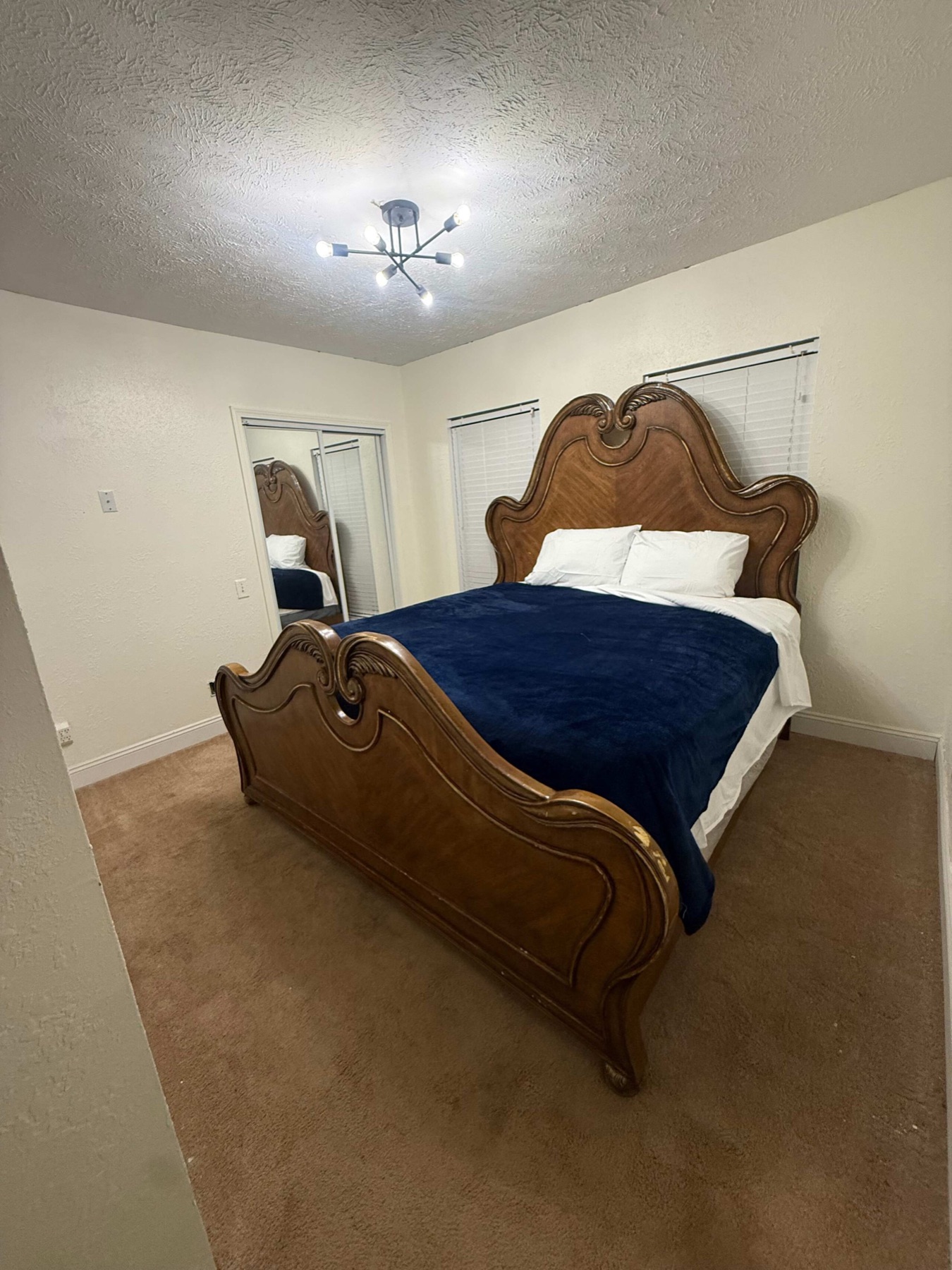 The king bedroom with a carved wooden headboard and navy blanket over white bedding.