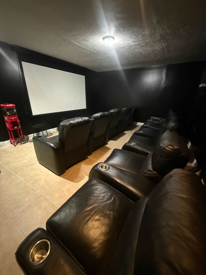 The private theater: two tiered rows of black leather reclining seats with cup holders facing a large projection screen, a red popcorn cart to one side.