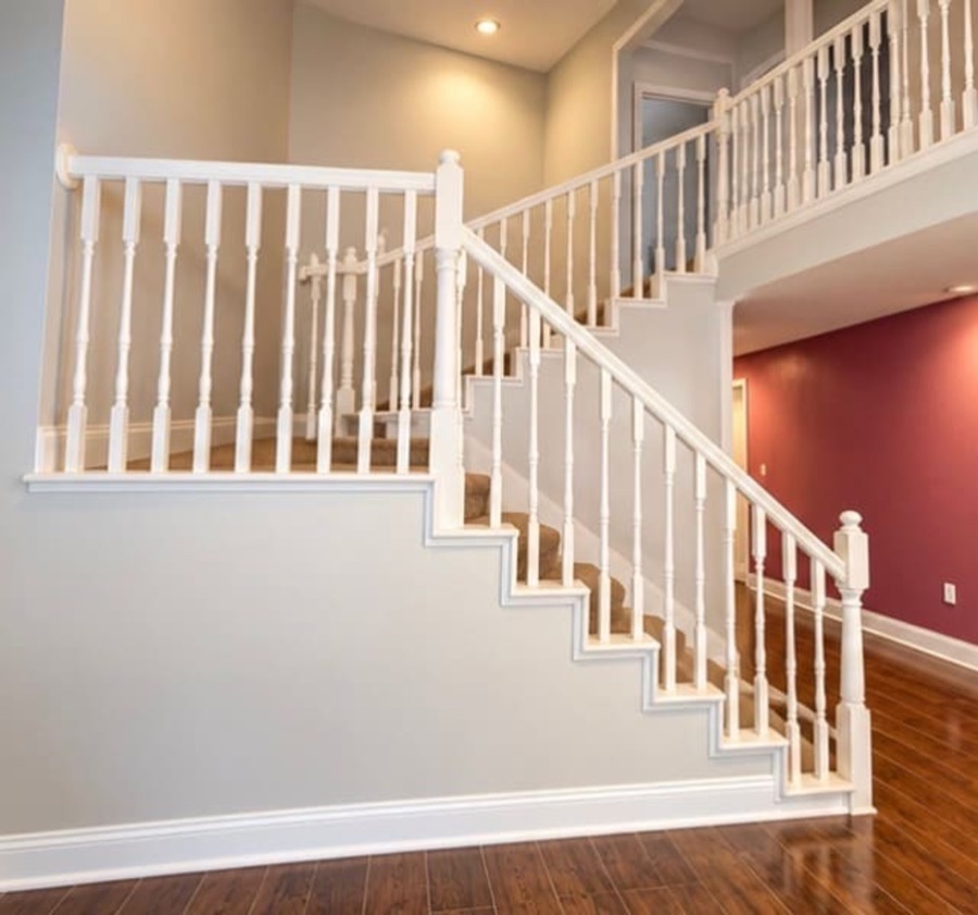 A white balustraded staircase rising to an open second-floor landing, with a deep red wall visible beyond.
